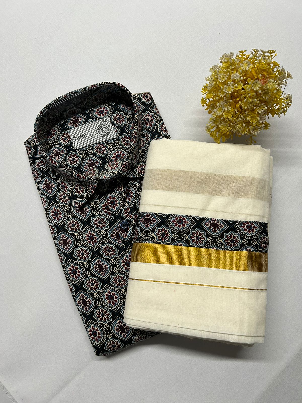 Folded black patterned shirt with a white saree with gold border on a light gray background