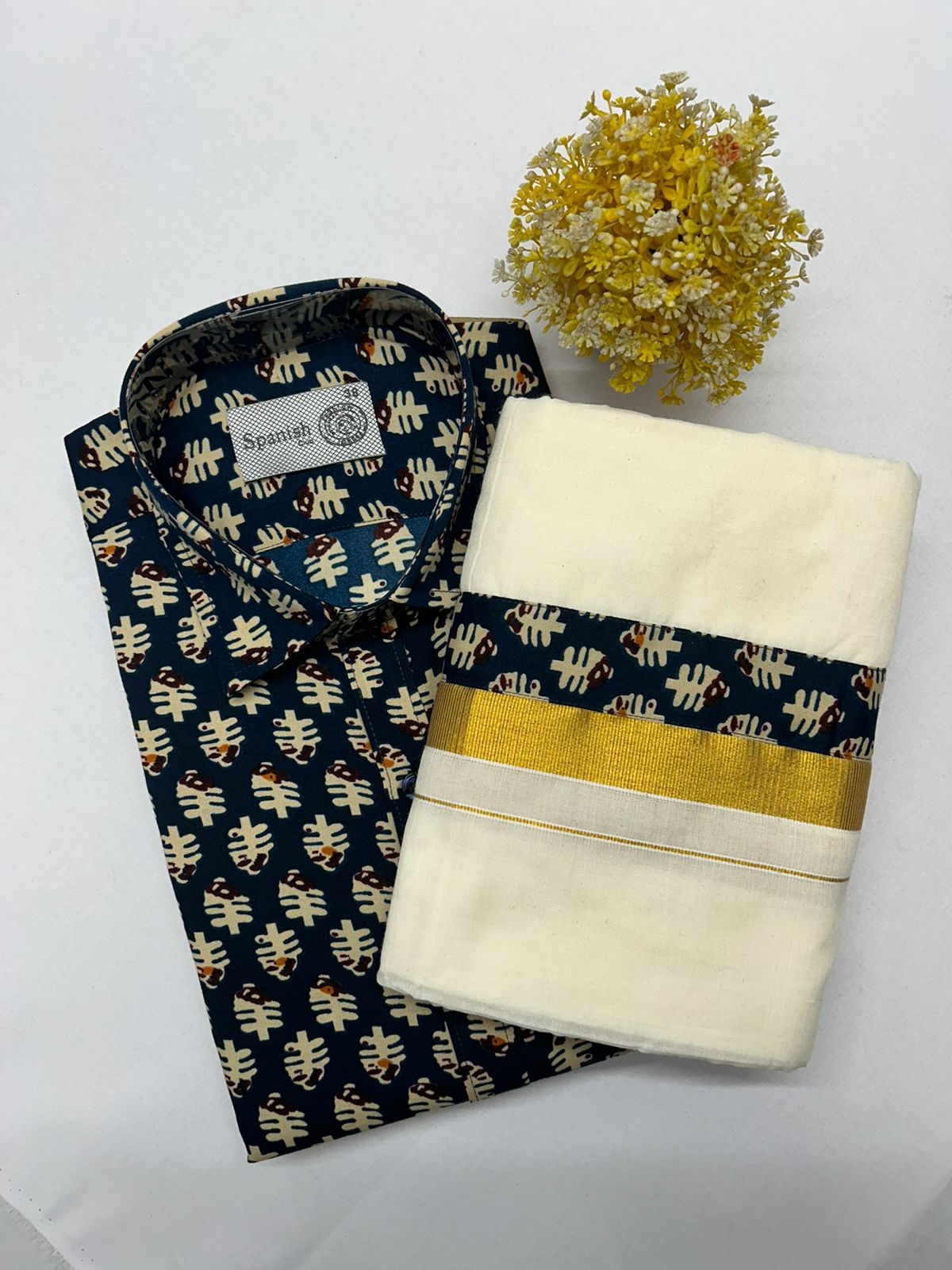 Folded patterned shirt and white towel with gold stripe on a light gray background