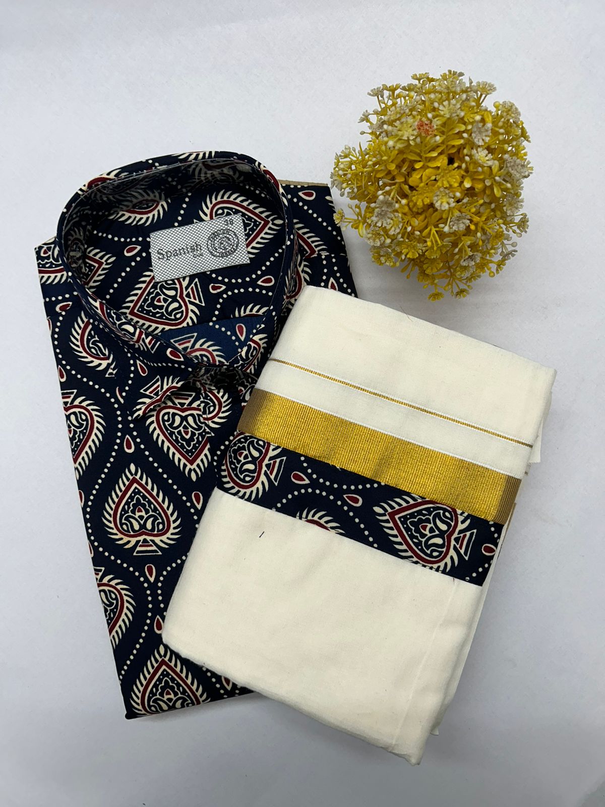 Folded patterned shirt and white pants with a yellow flower on a light gray background
