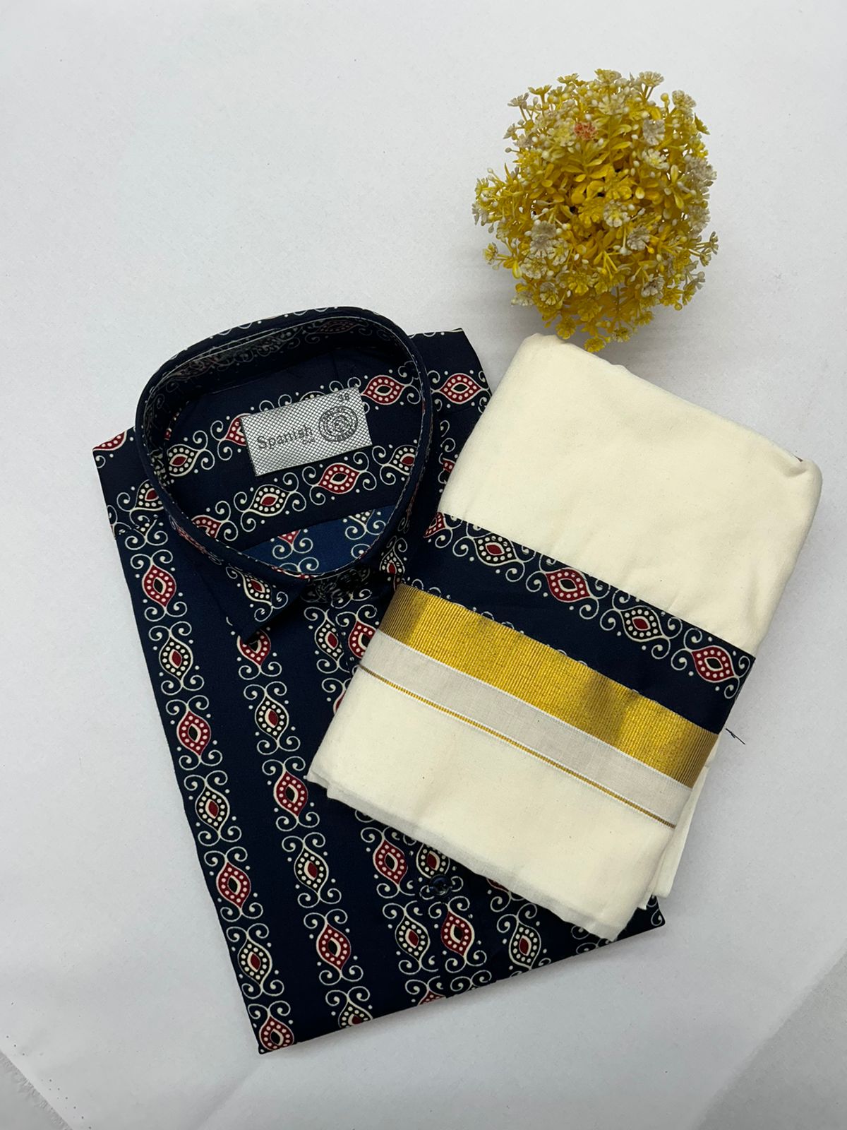 Navy blue shirt with pattern, white towel with gold band, and yellow flower on a light gray background