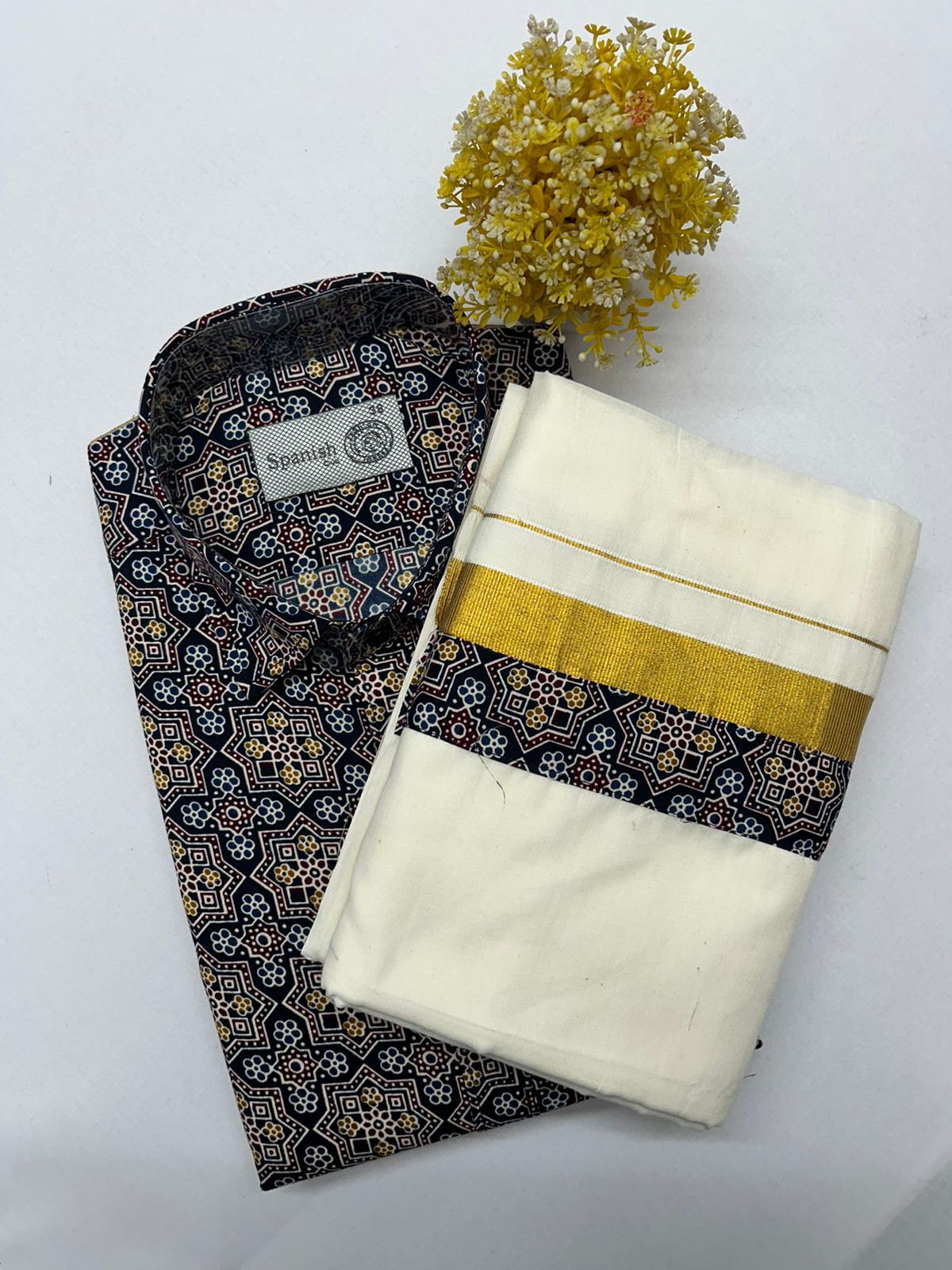 Folded black and gold patterned fabric next to a white saree with a gold border on a white background.